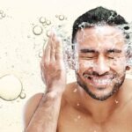 A happy man washing his face, representing skincare for men.